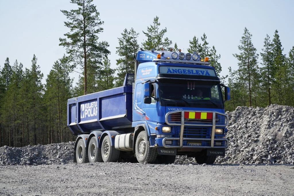 Kesäinen kuva maa-ainesten kuljettamiseen tarkoitetusta sinisestä kuorma-autosta, joka odottaa kuormaajaa ottoalueella.