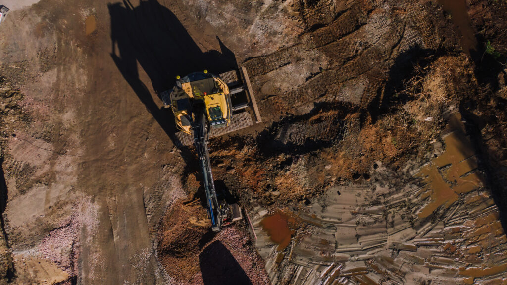Maanrakennusta ilmasta kuvattuna. Keltainen kaivinkone työskentelemässä suuremmalla rakennustyömaalla.