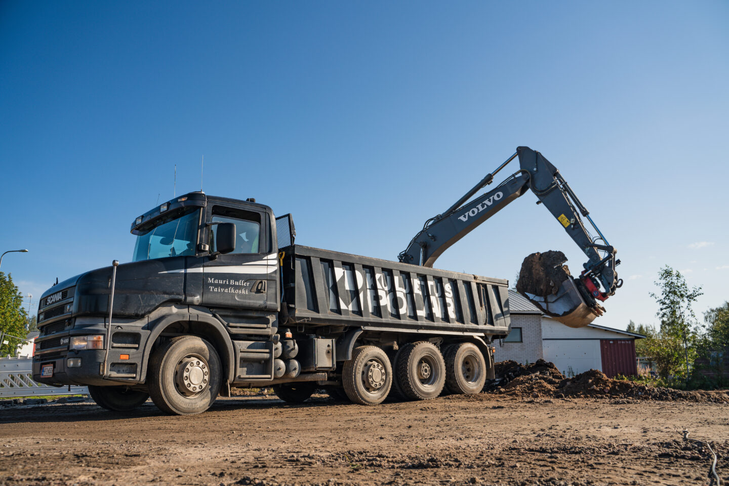 Kaivuutyöt: mustaa kuorma-autoa lastataan maa-aineksella rakennustyömaalla.